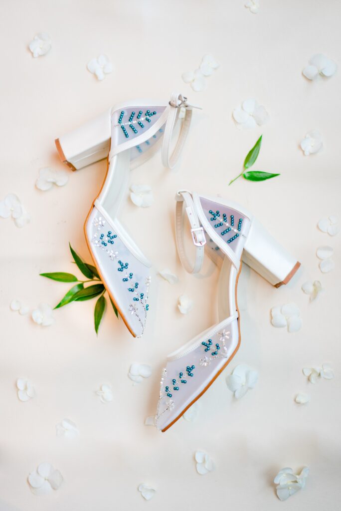 beaded white heels on a white background with flower petals