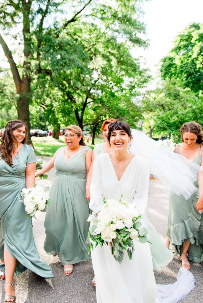 bride and bridesmaids in lightgreen walk through Lincoln Park and smile while holding white bouquets