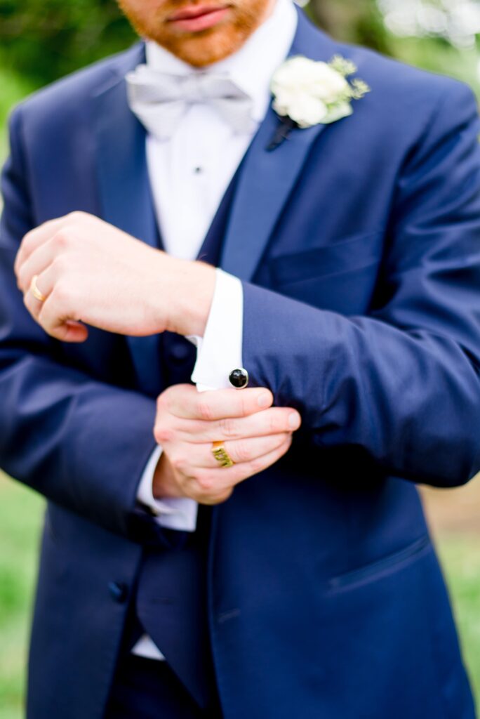 groom in navy suit fixes cufflink