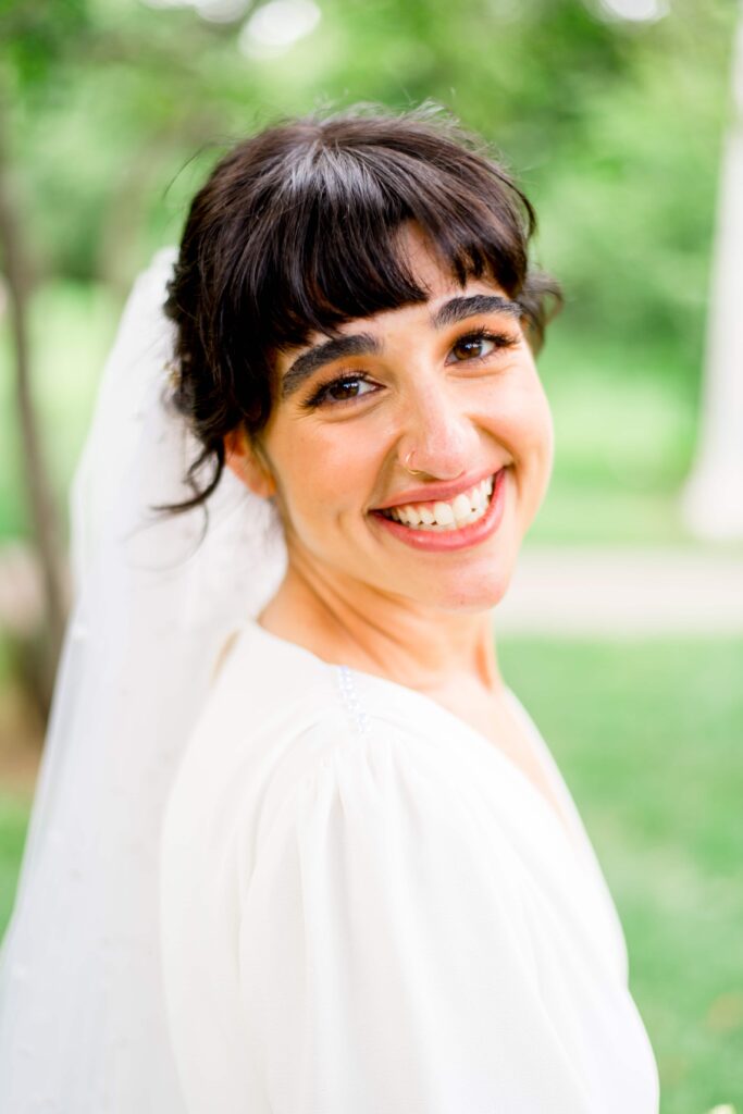 bride smiles in front of soft green trees in Lincoln Park
