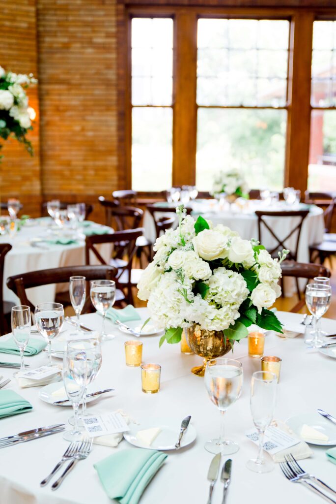 table setting at Cafe Brauer with white roses and hydrangeas, sage green napkins, and votive candles lit