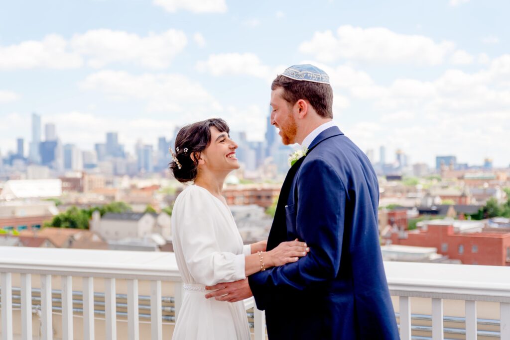 bride and groom smile at each other on the roof of Hyatt Place Wicker Park with the Chicago skyline behind them