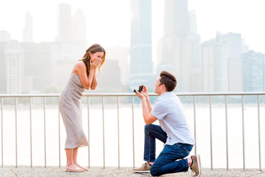 Man proposes to woman in front of the Chicago skyline at sunset in Olive Park. 