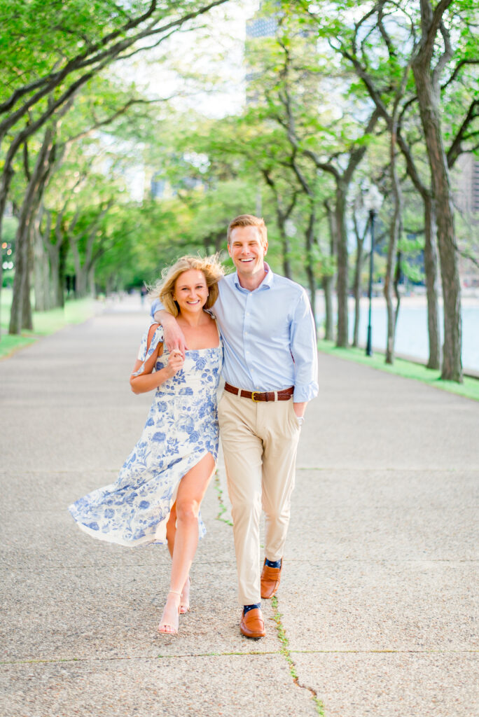 Man and woman in light blue outfits walk and smile on a tree lined path in Olive Park in downtown Chicago. 
