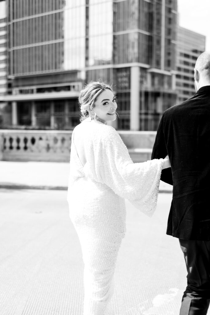 bride looking back smiling while groom walks her through downtown chicago on wedding day 