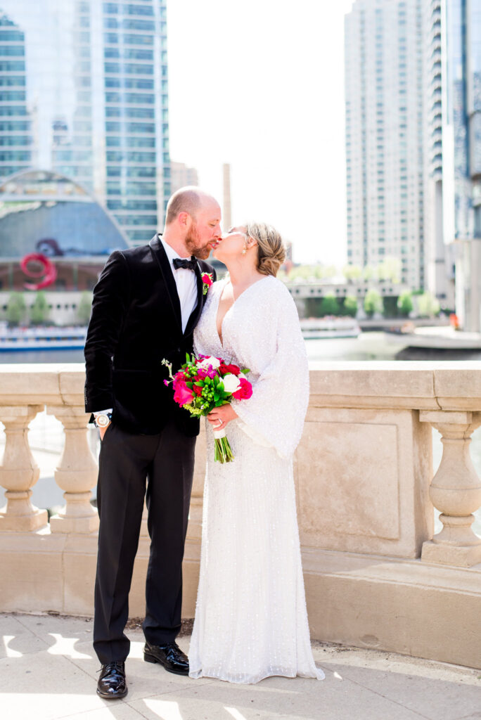 couple kissing and holding hot pink bouquet overlooking the Chicago River at wolf point 