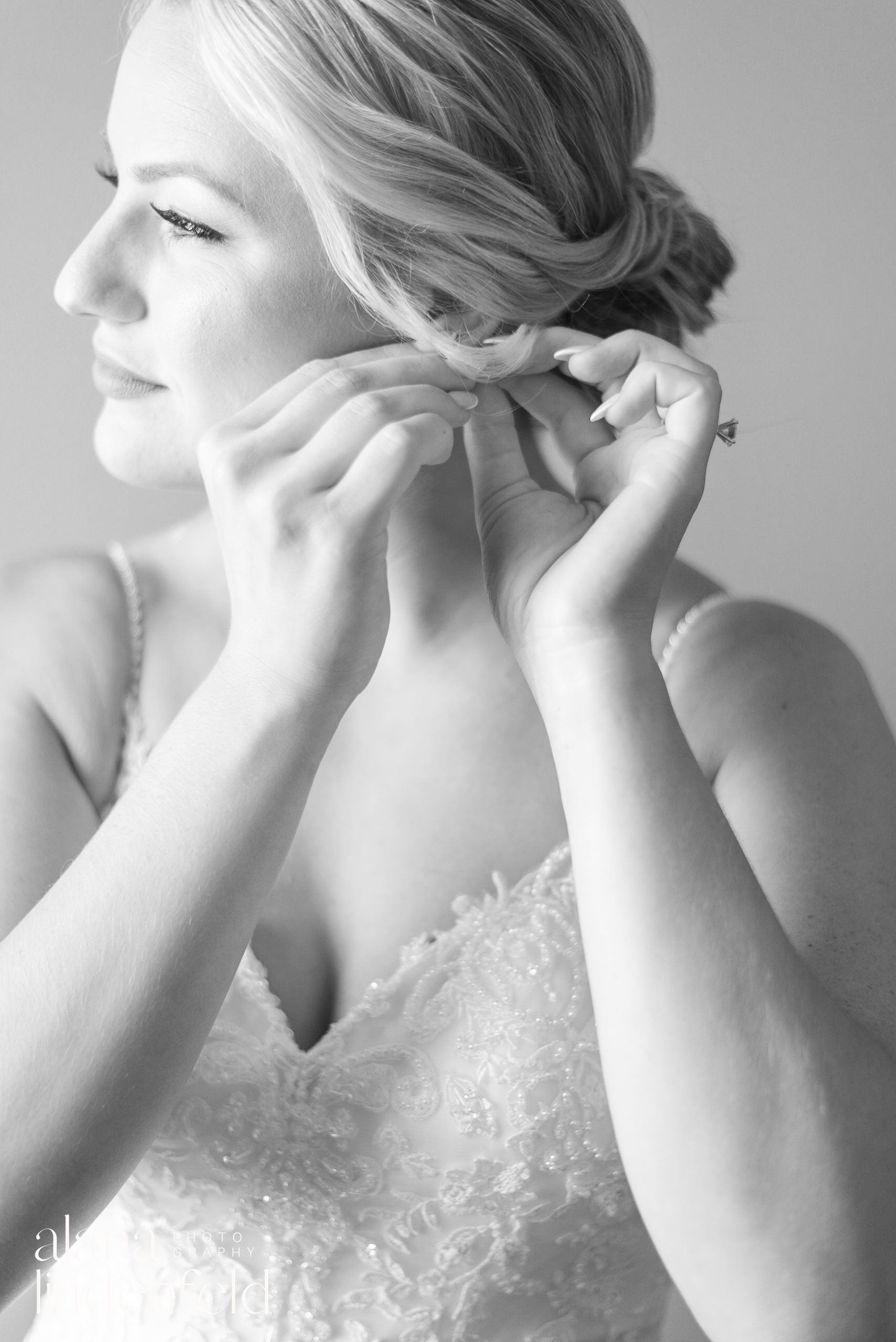 black and white bridal portrait putting earrings on