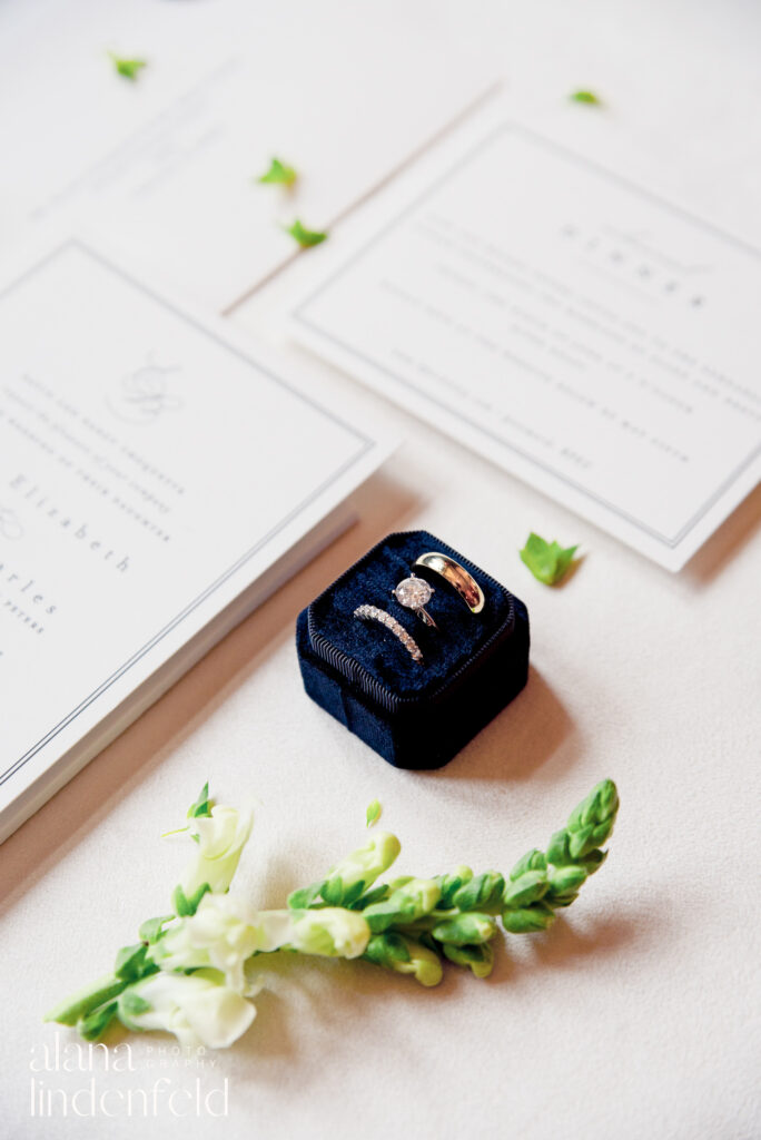 wedding and engagement rings in a black velvet ring box with white snapdragons
