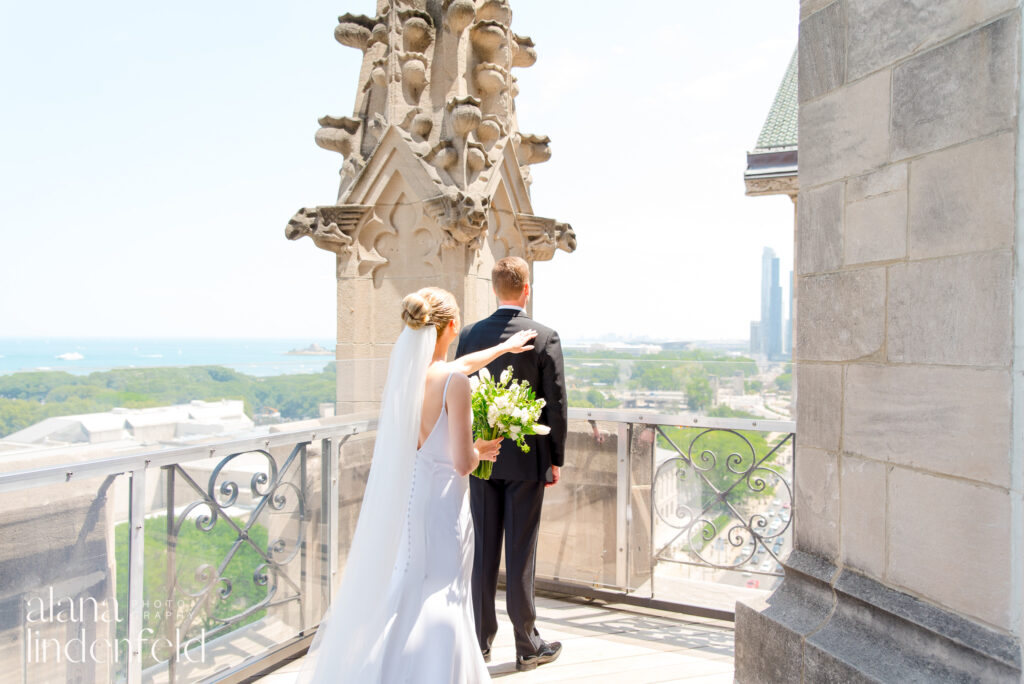 bride in a bun and long veil taps groom on shoulder before first look on roof of University Club of Chicago
