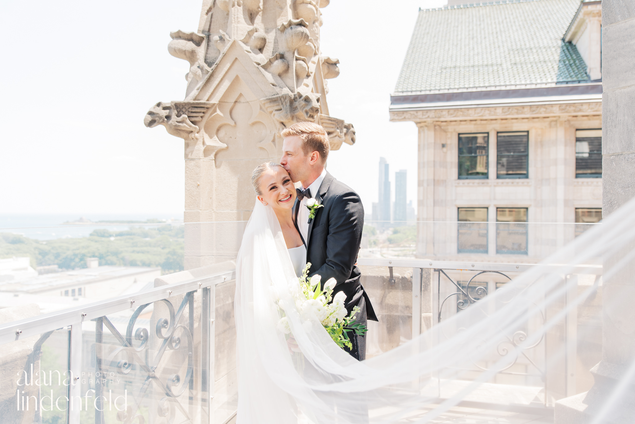 Groom kisses bride on cheek on rooftop of University Club Chicago in the summer