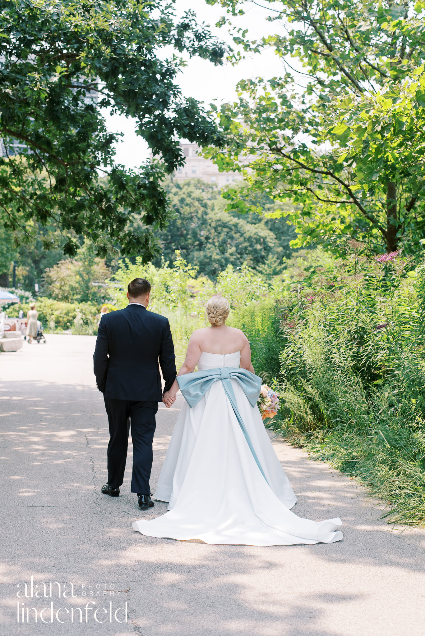 bride with blue bow on back of dress walking with groom through lincoln park zoo in chicago
