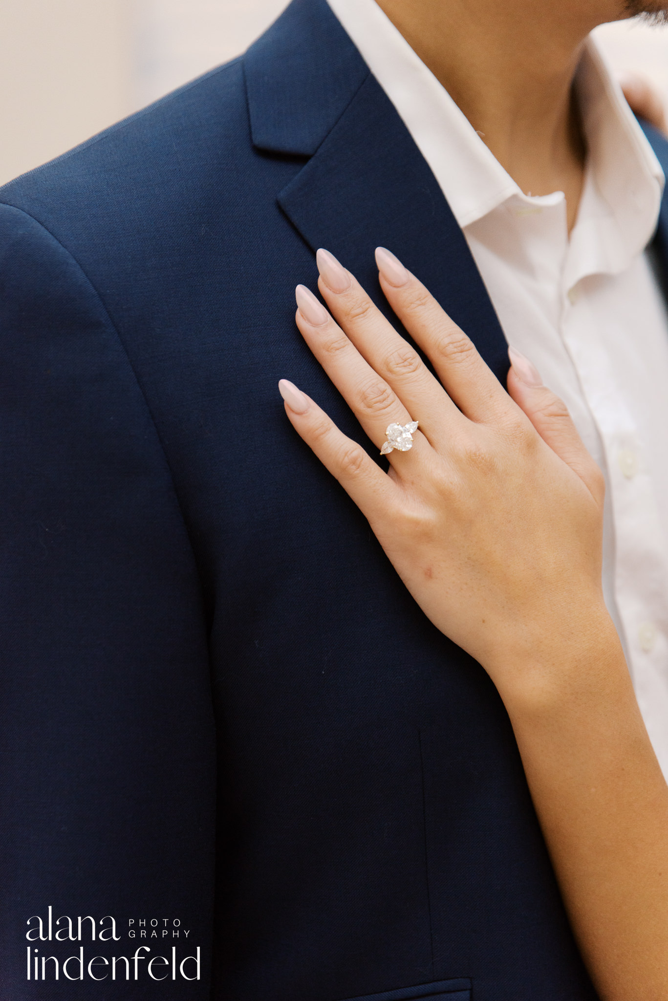 woman's hand with diamond engagement ring resting on partner's suit lapel 