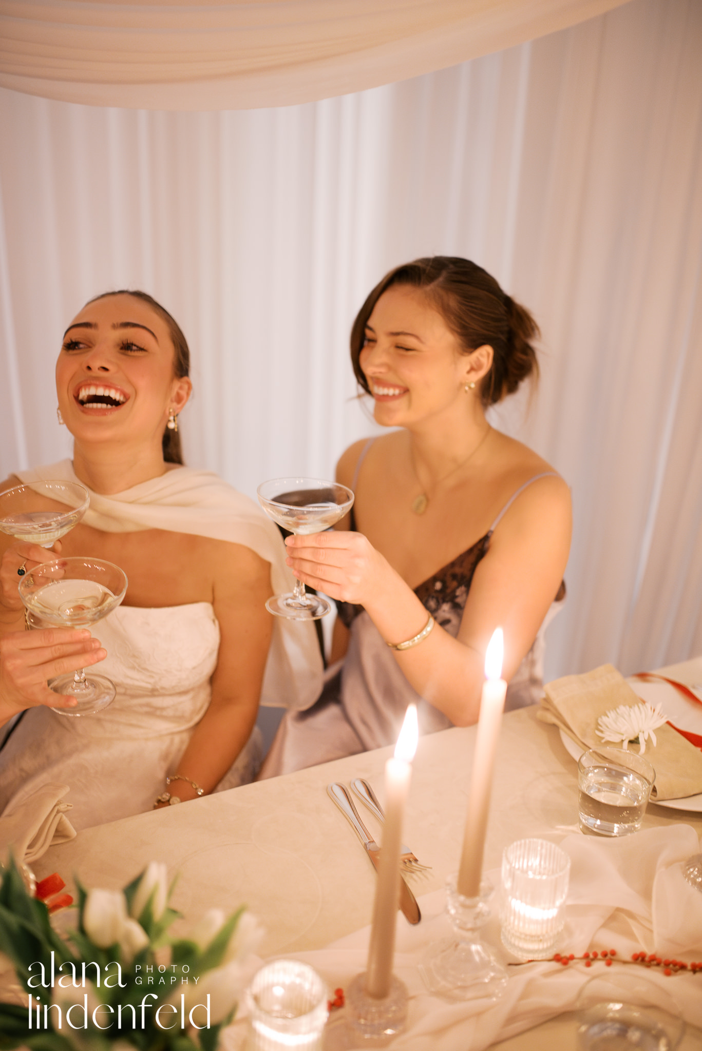 bride and bridesmaid laughing at candlelit dinner table 