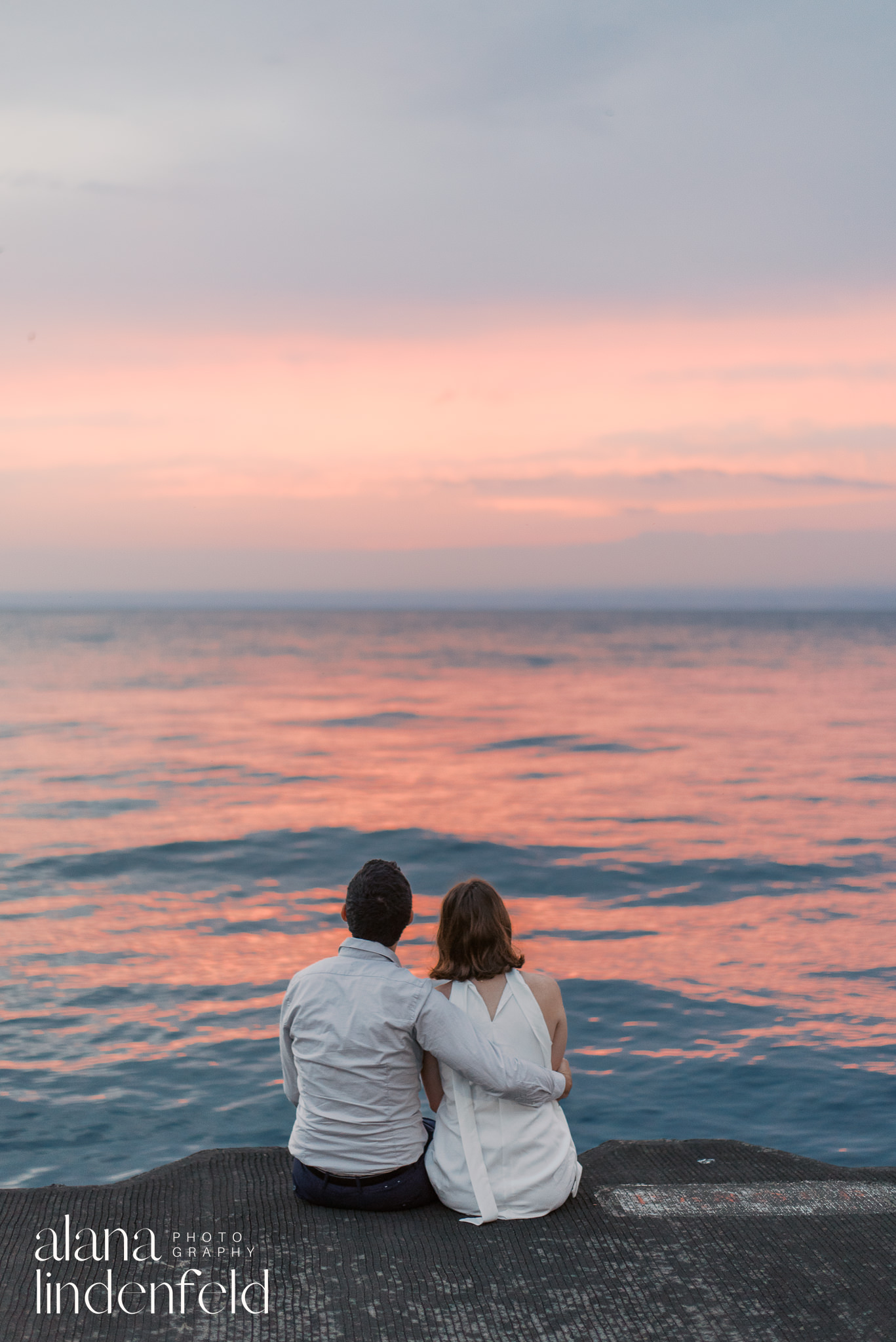 couple sitting on lake michigan edge watching the sunrise 