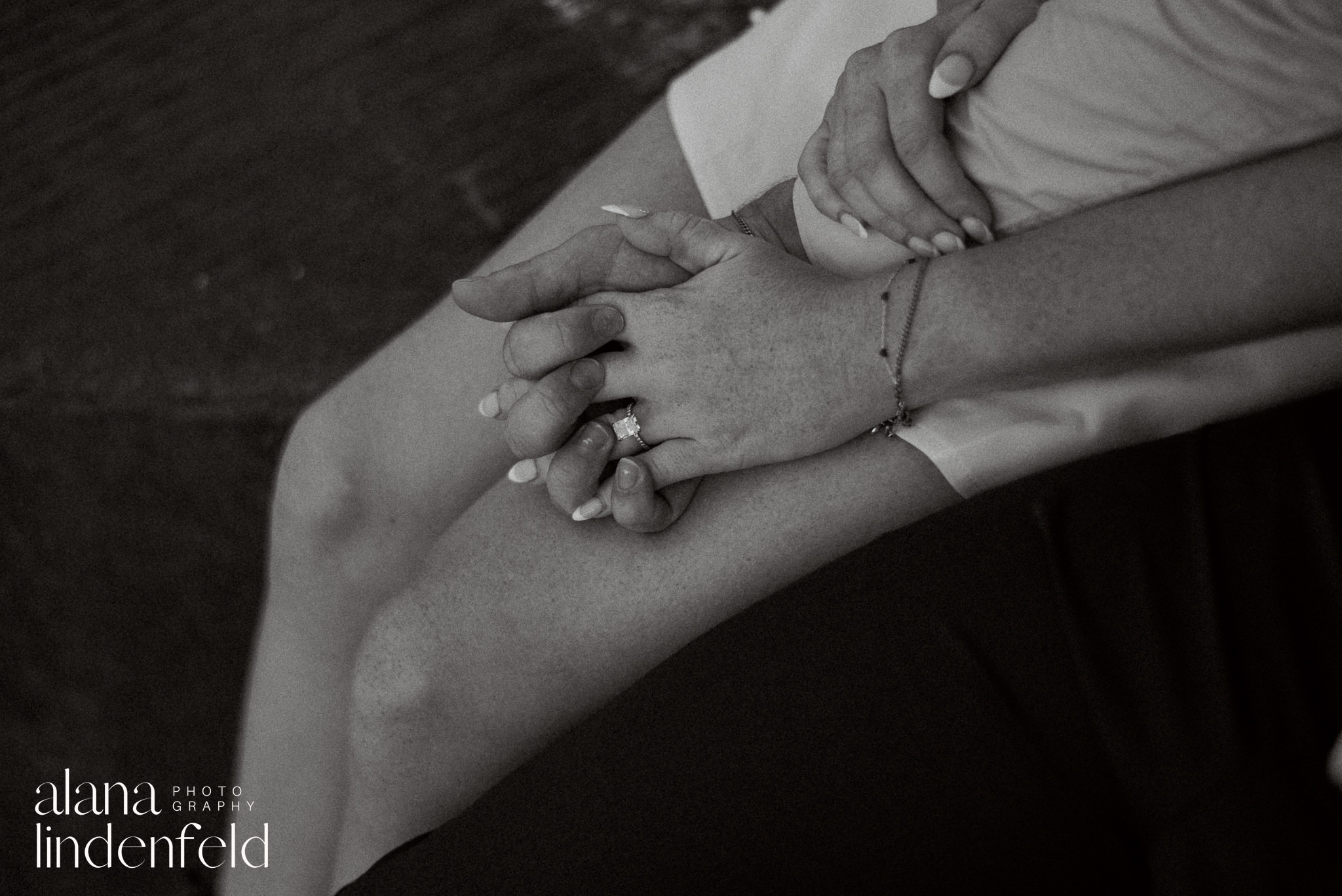 black and white film engagement photo of couple holding hands and showing engagement ring 