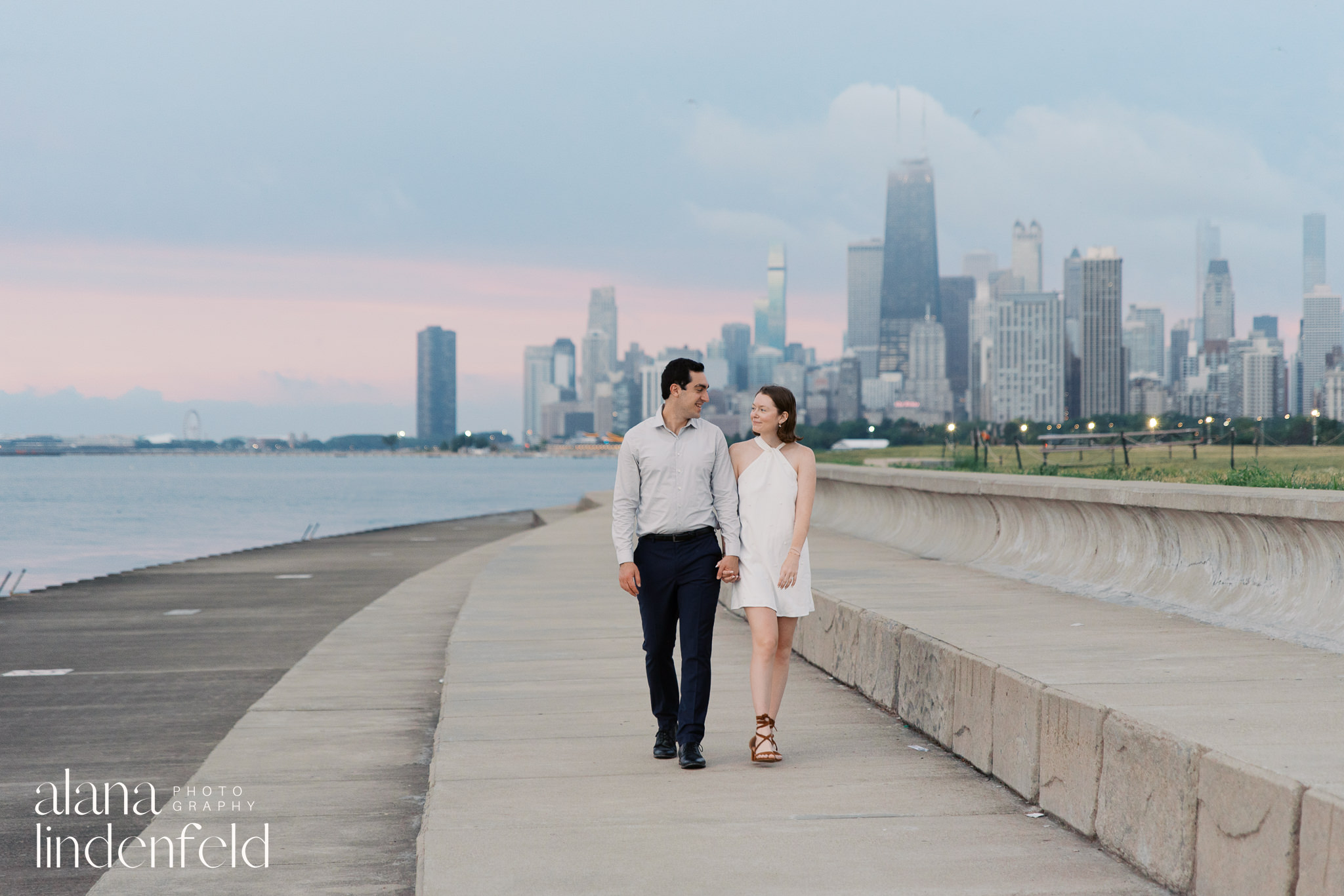 couple walking along Lake Michigan with Chicago skyline behind them at sunrise 