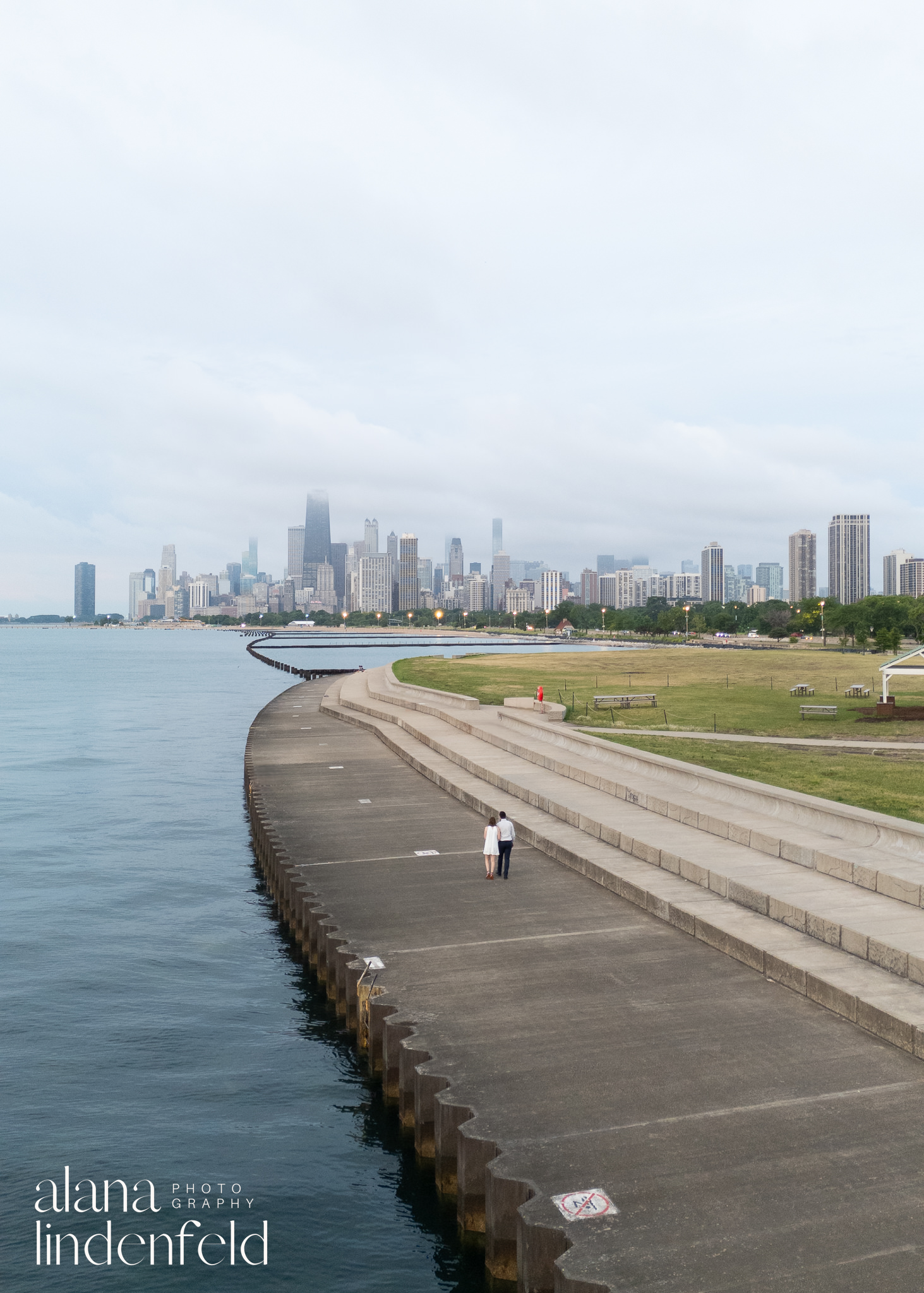 couple walking along Lake Michigan with Chicago skyline behind them at sunrise 