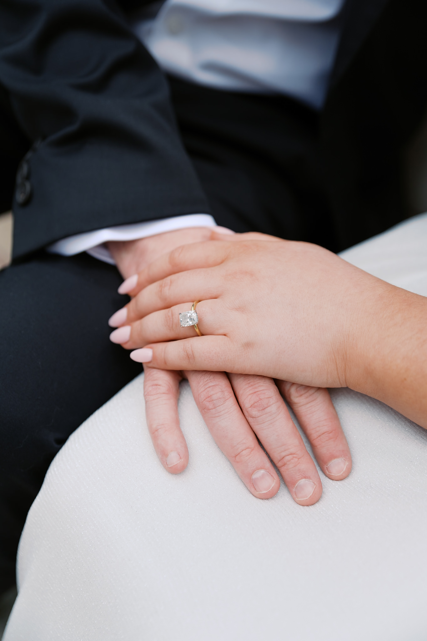 couples hands on top of each others' laps showing off engagement ring
