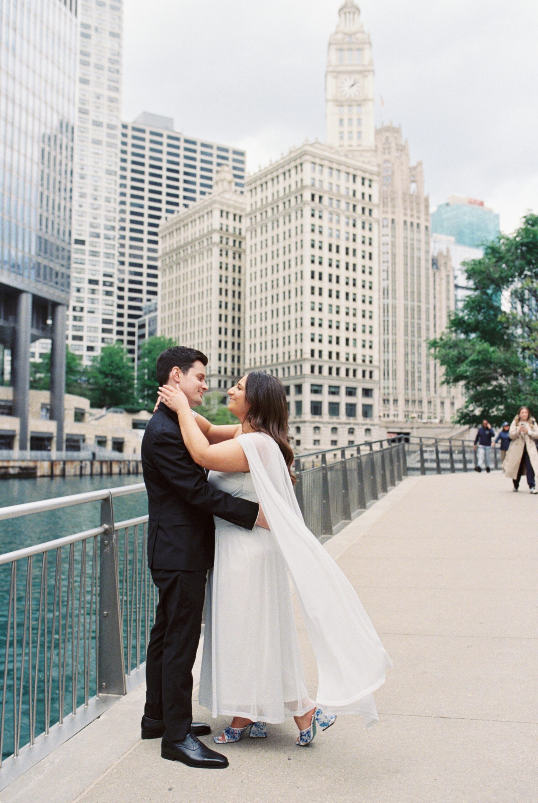 film photography of Chicago Riverwalk engagement picture with Wrigley Building behind a couple smiling at each other